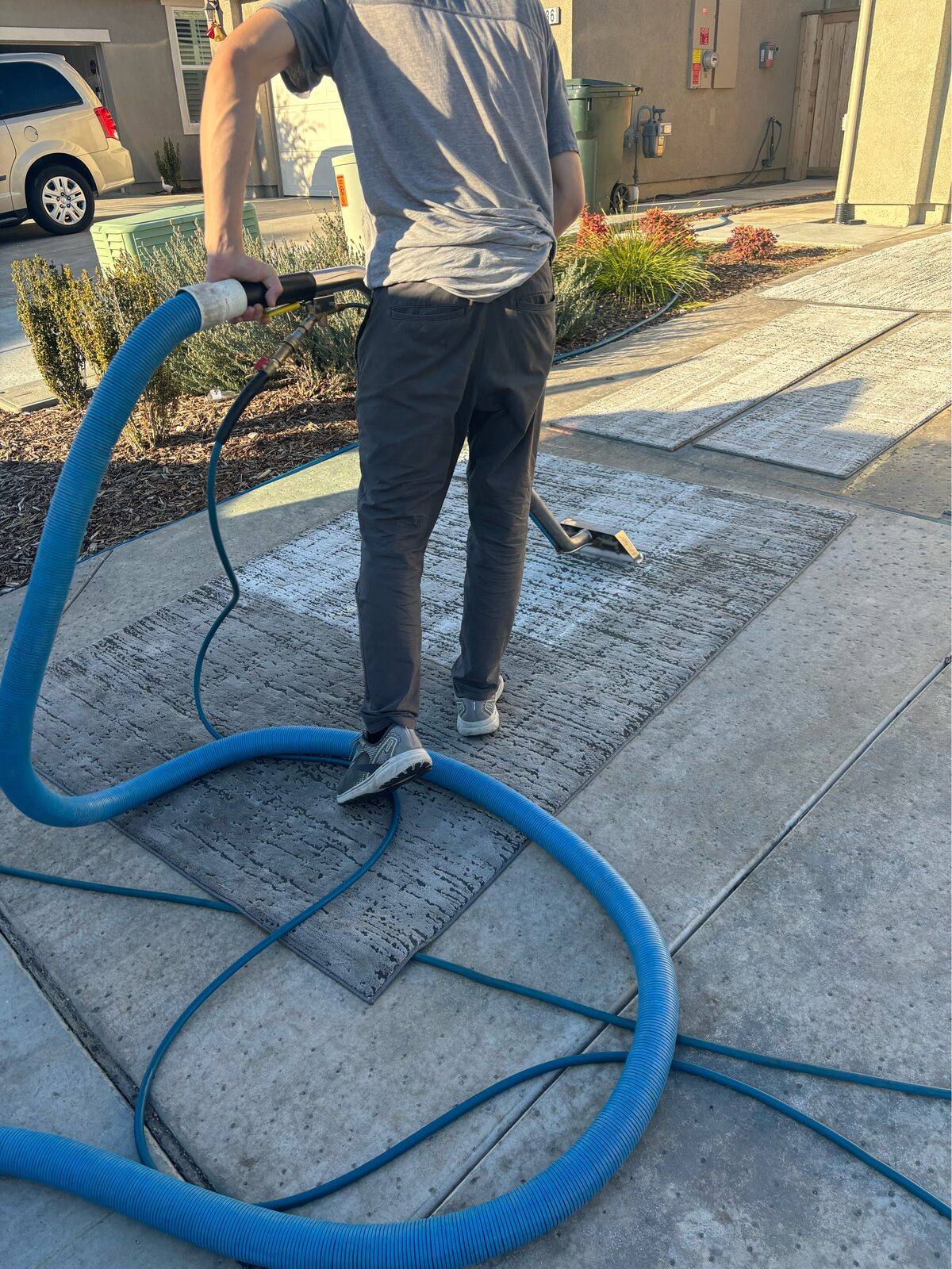 Technician cleaning an area rug on a driveway with truck-mounted equipment